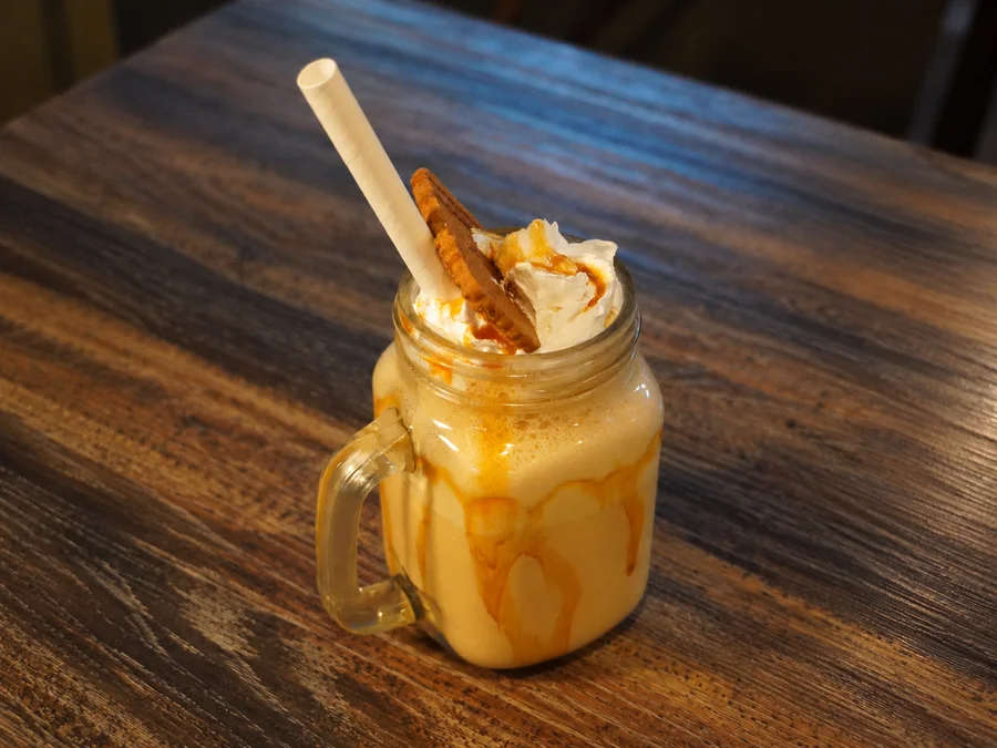 A creamy drink topped with whipped cream and a biscuit in a glass mug at Story Coffee House